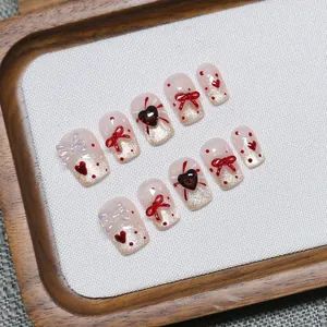 Faux ongles faits main avec nœud rouge, détails cœur et finition French œil de chat