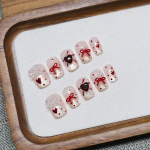 Faux ongles faits main avec nœuds 3D rouges, cœurs et pois sur base pailletée nue