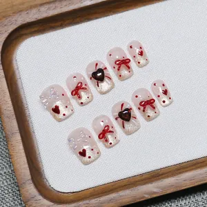 Faux ongles faits main avec dégradé pailleté rose, nœuds rouges et détails de cœur