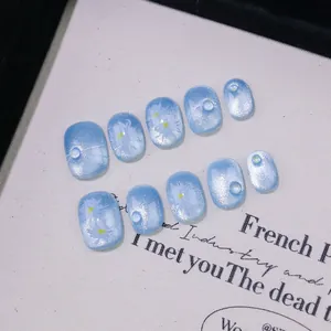 Detail of light blue cat-eye press-on nails with white daisies and pearl accents