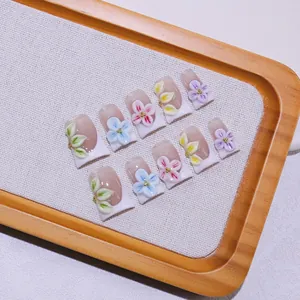Handmade 3D floral press-on nails with French tips on a rustic wooden tray display