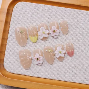 Handmade almond press-on nails with 3D floral accents and French tips on wooden tray