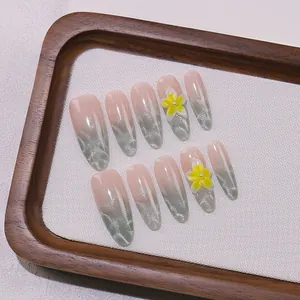 Detalle de uñas postizas almendradas con flores amarillas 3D y degradado de purpurina