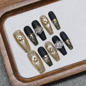 Handmade press-on nails with black matte design, gold foil, and rotating snowflakes