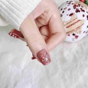 Unghie finte rosa cat-eye con fiocco dorato e ghirlanda natalizia di perle e strass