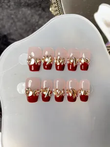 Détail macro d'ongles faits main avec French rouge, perles et strass dorés brillants