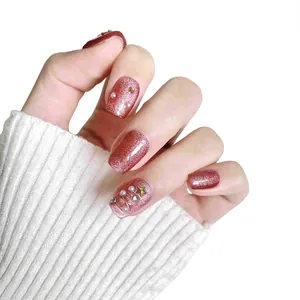 Unghie finte rosa cat-eye con perle e stelle dorate su sfondo di maglione bianco