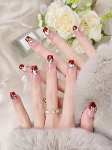 Gros plan sur des faux ongles faits main bordeaux avec strass et détails en perles