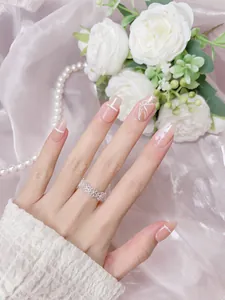 Macro detail of nude pink press-on nails with white bows, pearls, and silver glitter lines