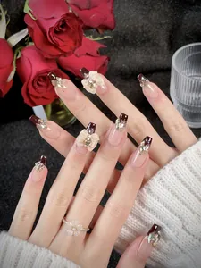 Dettaglio di unghie finte bordeaux fatte a mano con fiori 3D e accenti di glitter