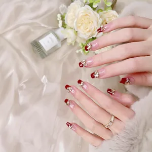 Faux ongles faits main, pointes rouges, cristaux et dorures sur un fond en soie élégante