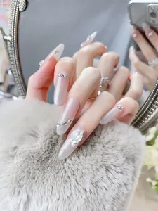 Close-up of almond-shaped press-on nails with pink gradient and sparkling rhinestones