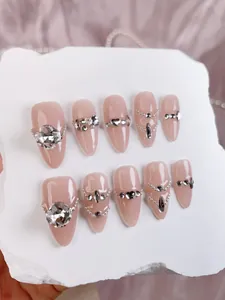 Detailed view of handmade nude almond press-on nails with luxury crystals and heart gems