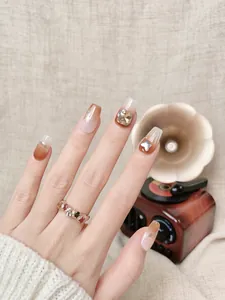 Macro shot of amber gradient press-on nails with metal butterfly and square rhinestones