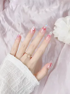 Detail of pink gradient press-on nails with 3D floral accents and gold cherry blossom ring