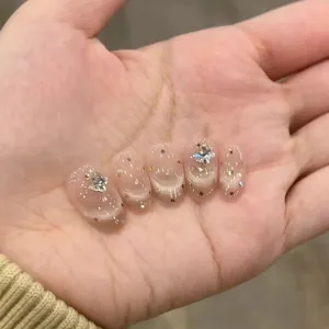 Detail showing five nude pink cat-eye press-on nails with silver rhinestone accents
