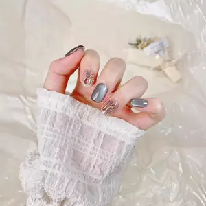 Faux ongles œil de chat argentés avec paillettes champagne et strass roses sur fond beige