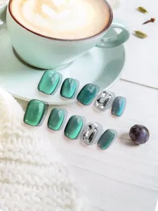 Dettaglio di unghie finte cat-eye verde smeraldo con glitter argento e strass lucidi