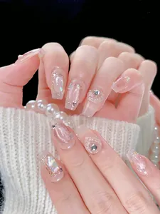 Detailed view of pink cat-eye press-on nails with pearls and shell textures on fingers
