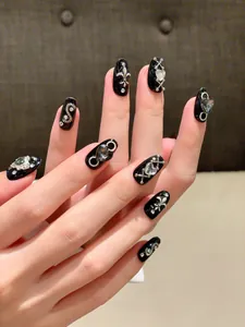 Detail of punk style black press-on nails with silver gothic charms and sparkling rhinestones