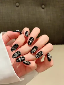 Detail of handmade goth black press-on nails with silver metallic cross and heart charms