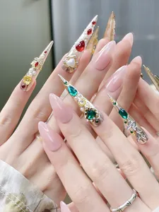 Detail of luxury press-on nails with red emerald gems and gold floral accents