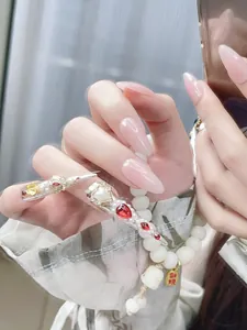 Detail of luxury stiletto press-on nails with red gems, pearls and golden vintage accents
