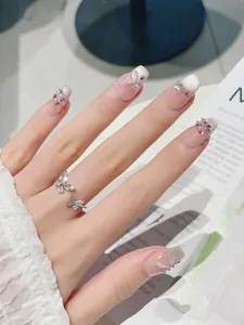 Detail of nude gradient press-on nails with 3D butterfly charms and pearl accents