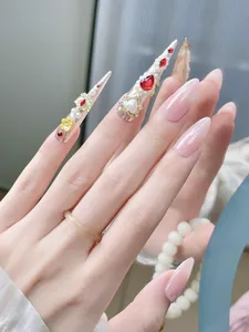 Detail of luxury stiletto press-on nails with 3D gold flowers, pearls and red rhinestones