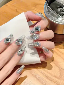 Detailed close-up of handmade long coffin nails with silver glitter, rhinestones and pearls