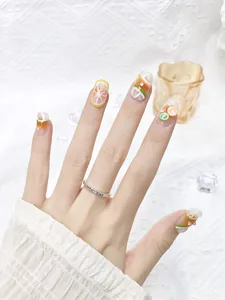 Detail showing handmade 3D fruit press-on nails with orange and lime slices and rhinestones