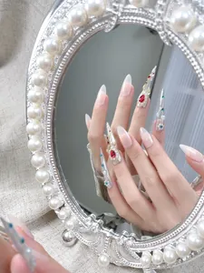 Makroansicht handgefertigter Stiletto Nägel mit roten Edelsteinen und Perlenspiegel