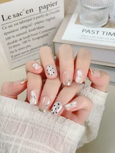 Détail d'ongles faits main avec pointes françaises argentées, nœuds et pois noirs