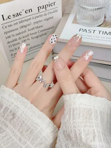 Détail de faux ongles roses avec pointes argentées, nœuds 3D et bague papillon