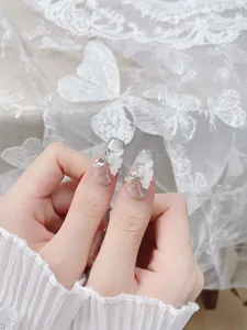 Detalle de uñas postizas hechas a mano con alas de mariposa 3D, perlas y diamantes