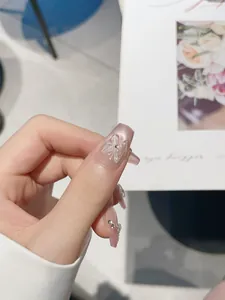 Dettaglio di unghie finte fatte a mano con farfalla 3D, perle e effetto cat-eye