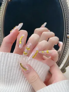 Gros plan d'ongles faits main en amande avec gemmes de cœur dorées et perles argentées