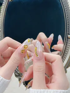 Détails de faux ongles roses avec fleurs d'ambre, strass dorés et perles de décoration