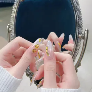 Faux ongles amande faits main avec strass jaunes et feuilles d'or sur base nude