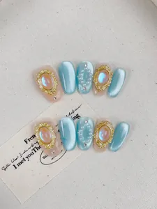 Détail d'ongles œil-de-chat bleus avec pierres aurora, perles et cadres dorés en relief