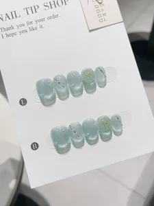 Detail of light blue cat eye press-on nails with pearls and gold butterfly charms