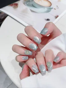 Macro view of blue-green cat eye press-on nails with white pearls and golden bows
