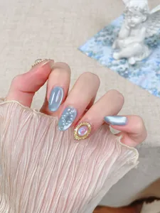 Détail de faux ongles œil de chat bleu avec perles et pierres précieuses dorées