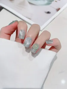Detail of Morandi green cat eye press-on nails with pearl and golden bow accents