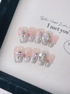 Macro detail of handmade blush press-on nails with 3D rhinestones and butterfly patterns