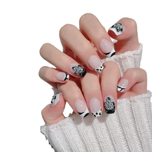 Faux ongles faits main noir et blanc avec fleurs 3D et strass brillants sur modèle