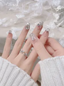 Detailed view of French gradient press-on nails with 3D butterfly charms and crystal accents