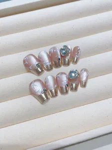 Detail of pink pearl press-on nails with gold French tips and rhinestone accents