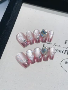 Macro shot of handmade press-on nails with pink pearls, blue rhinestones, and leaf art