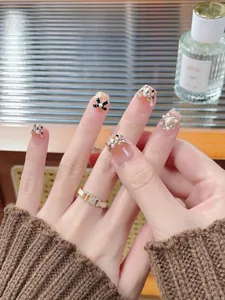 Detail of nude pink press-on nails with black bows, pearls and gold glitter accents